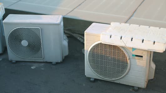 Two outdoor air conditioner units on the roof with one covered in ice